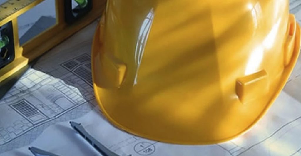 Un casco di protezione giallo e un compasso su un disegno tecnico.